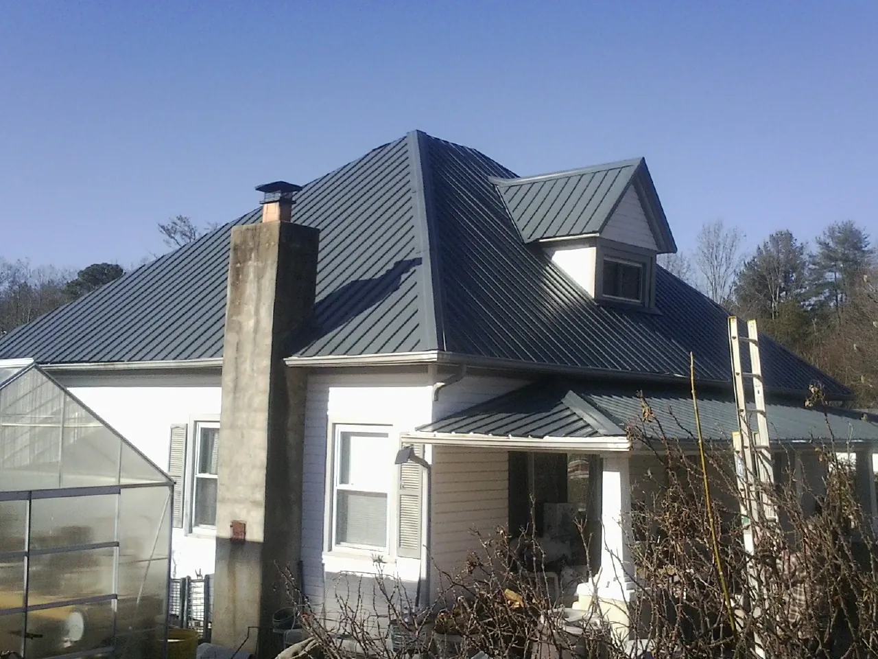 Dark blue standing seam metal roof on a white farmhouse with dormer — Slate & Tile Roof Repair by Roofing Brothers in Preston
