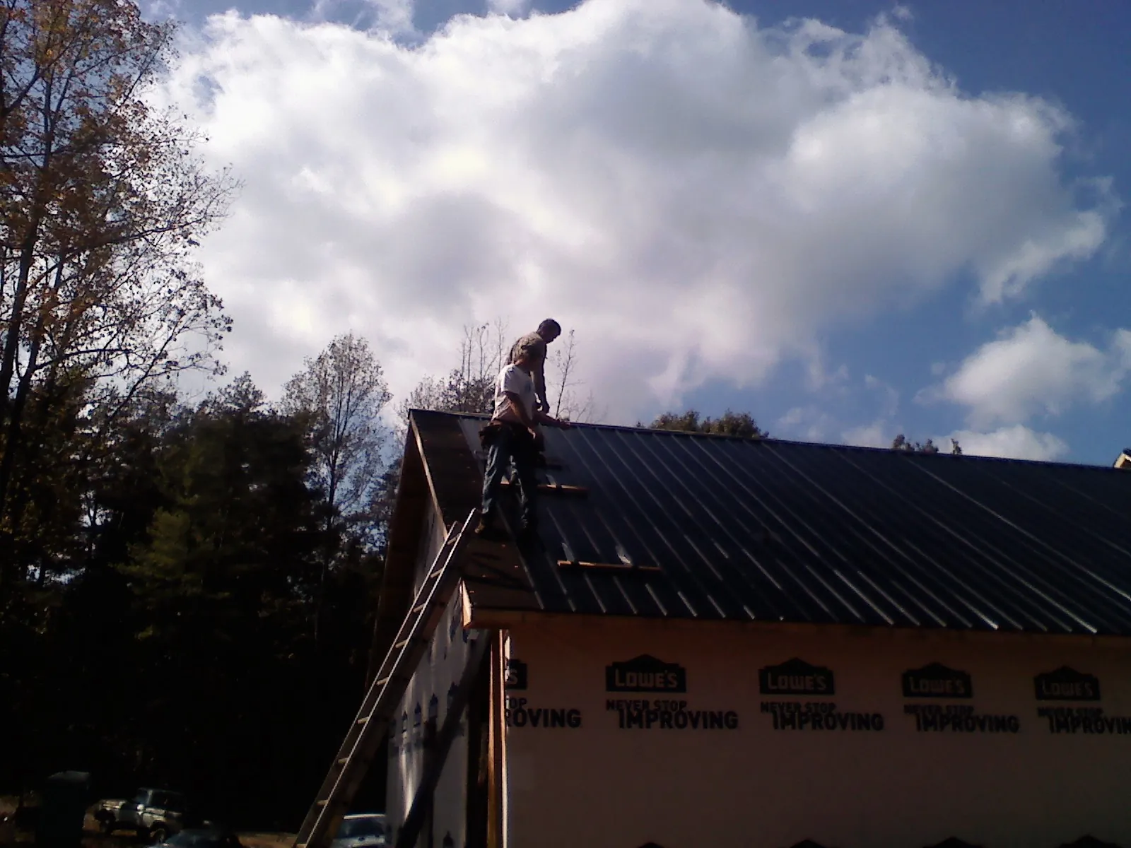 Roofer fastening dark metal panels high against a cloudy sky, from a Roof Inspection job in Preston